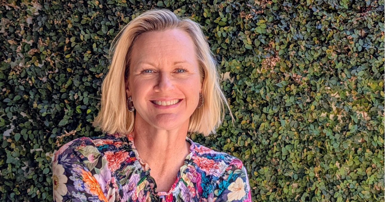 Jacqueline Smith, founder of Bloom Eden, smiling in front of a leafy green hedge.